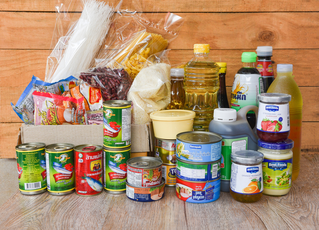 Donations box with canned food on wooden table background / pasta canned goods and dry food non perishable with oil rice noodles spaghetti macaroni donations food